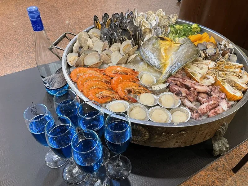 龍福山莊海鮮痛風鍋,大鍋內鋪滿蛤蜊、白蝦、透抽與鮮魚,旁邊是倒好的藍眼淚葡萄酒。